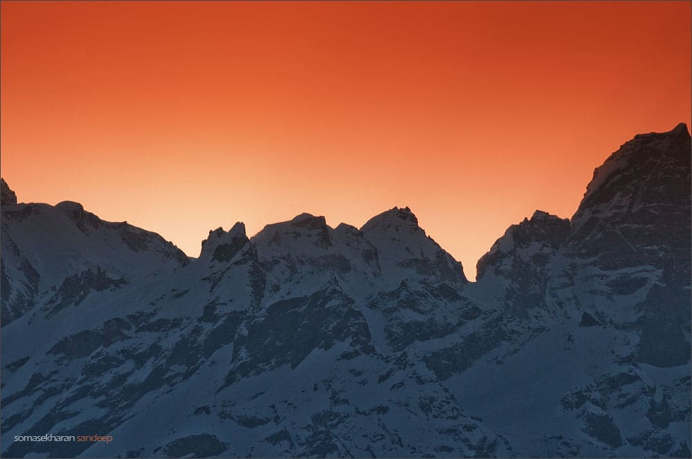 The sun rises behind a wall of snow and rock